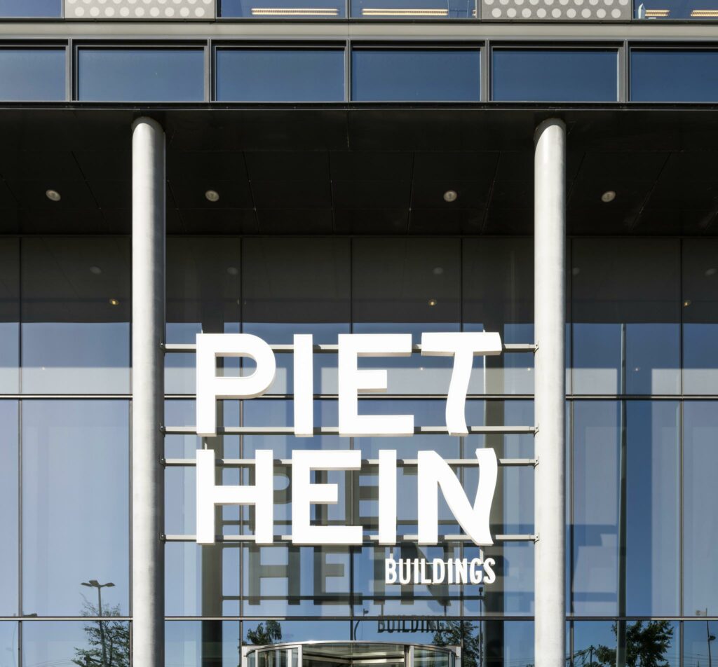 Vooraanzicht van de ingang van het Piet Hein Buildings-gebouw met grote witte letters op de gevel.